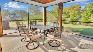 Un patio couvert avec une table et des chaises, de grandes fenêtres et une vue sur une maison et des arbres.