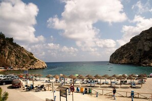 Une plage avec des parasols, des chaises longues et une falaise rocheuse.