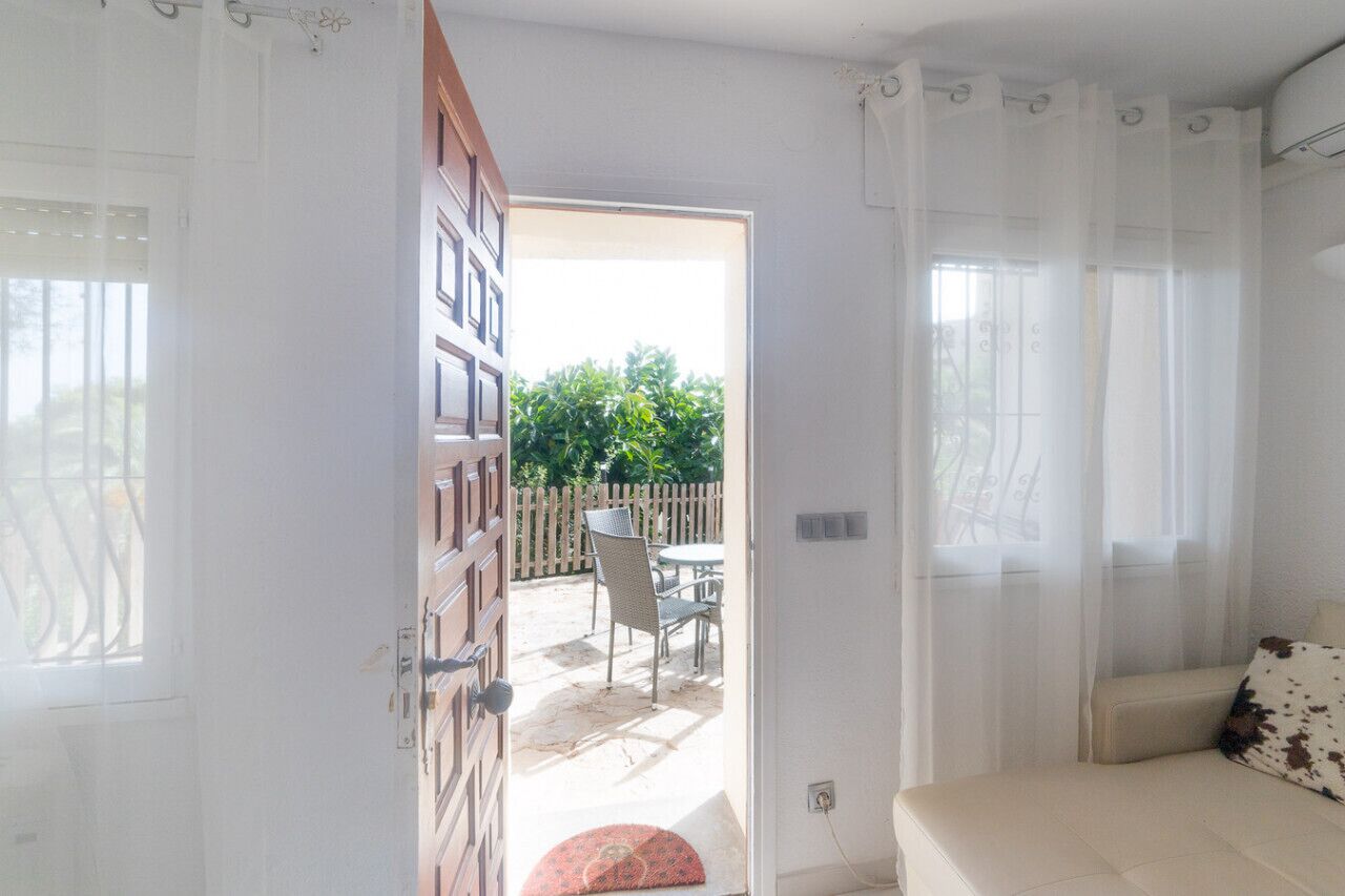 Une chambre à coucher avec un lit, une fenêtre ornée de rideaux légers et une vue sur une terrasse extérieure avec une table et des chaises.