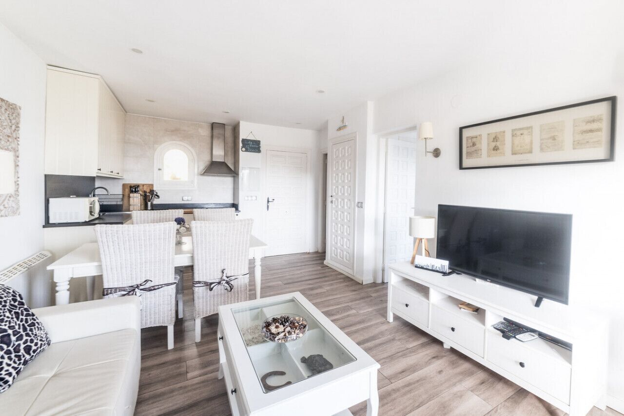 Un salon moderne et bien éclairé, avec un coin repas, un téléviseur et une cuisine en arrière-plan.