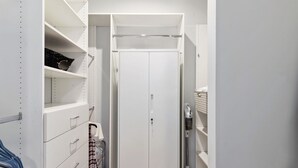 A walk-in closet with open shelves, a closed door, and a vacuum cleaner on the right.