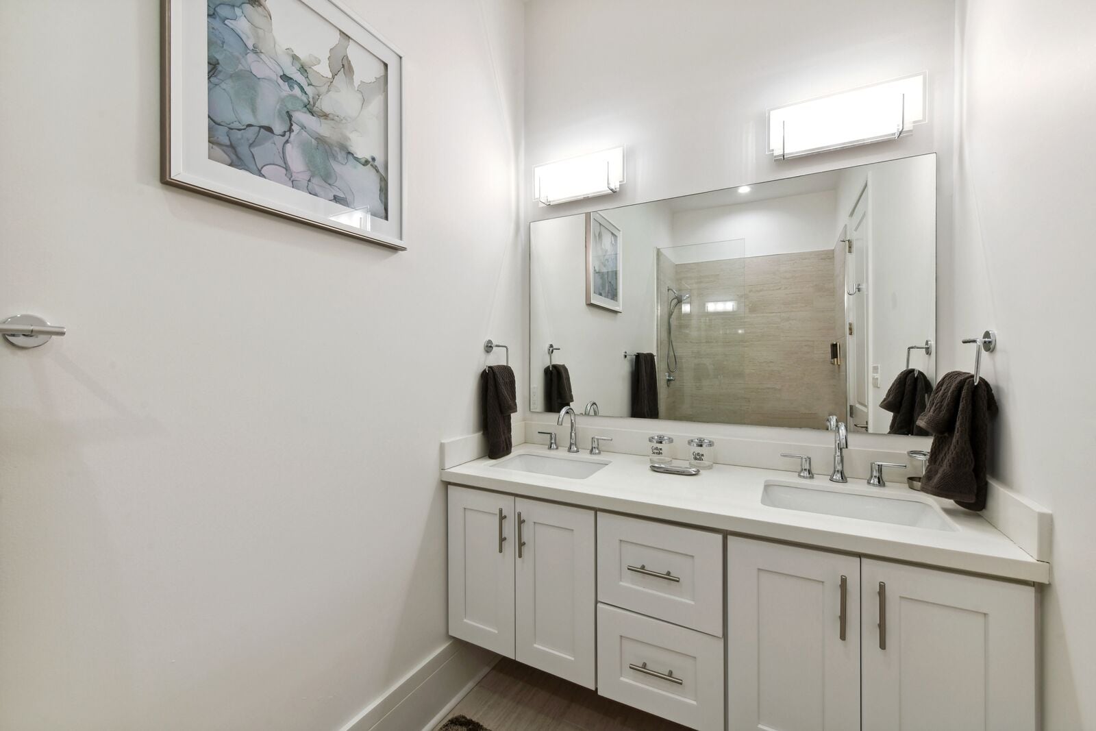 Un baño moderno con dos lavamanos, un espejo grande y un cuadro abstracto enmarcado en la pared.