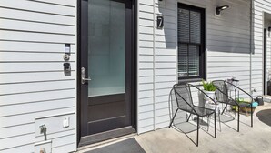 A modern house with a black front door, a small patio with a table and chairs, and a window with blinds.