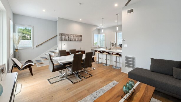 A modern living room with a dining area, a kitchen, and a staircase.
