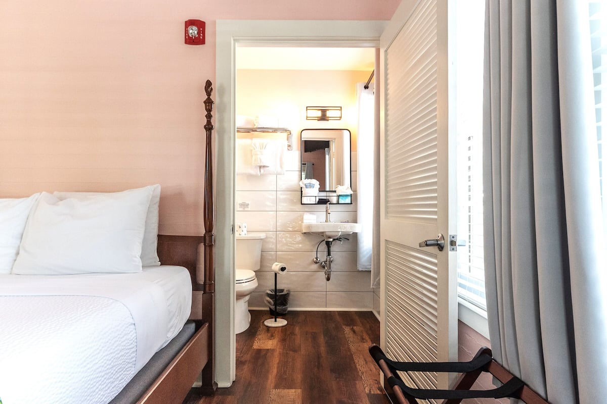 A hotel room with a bed, a bathroom with a toilet, sink, and mirror, and a window with curtains.