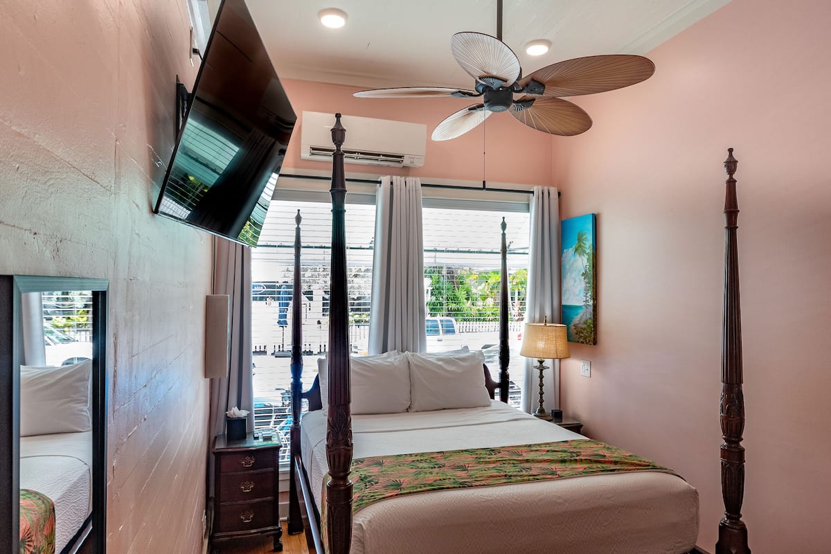 A bedroom with a bed, a ceiling fan, a TV mounted on the wall, and a window with curtains.