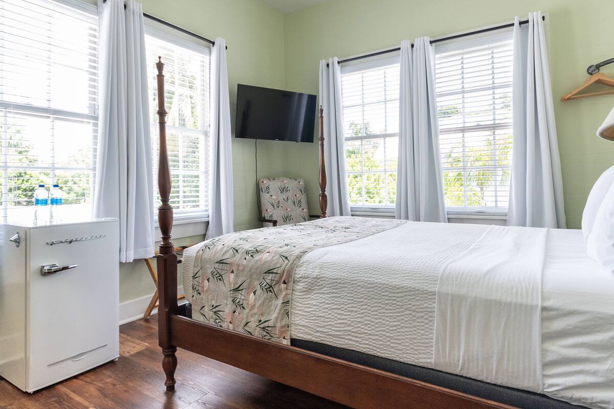 A bedroom with a bed, a wooden wardrobe, a television mounted on the wall, and a chair.