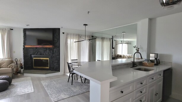 A modern kitchen with a large island, white cabinetry, and a built-in oven. There is a dining area with a table and chairs, and a living room with a sofa and a fireplace. - Newly Renovated 2BR - walk to lift;  walk to Stratton Village; easy parking (Stratton)