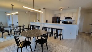 A modern kitchen with white cabinets, a black refrigerator, and a microwave. There is a dining area with a round table and black chairs. - Newly Renovated 2BR - walk to lift;  walk to Stratton Village; easy parking (Stratton)