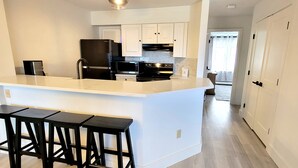 A modern kitchen with a central island, black appliances, white cabinetry, and a bar stool area. - Newly Renovated 2BR - walk to lift;  walk to Stratton Village; easy parking (Stratton)