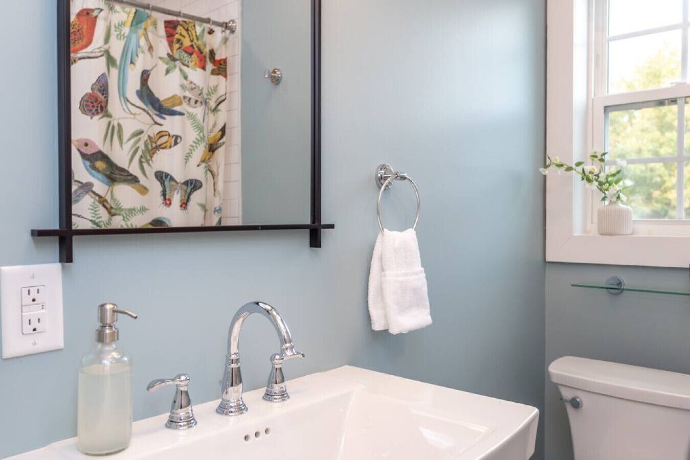 Une salle de bain avec un lavabo blanc, trois robinets, un miroir, un porte-serviettes et des toilettes.