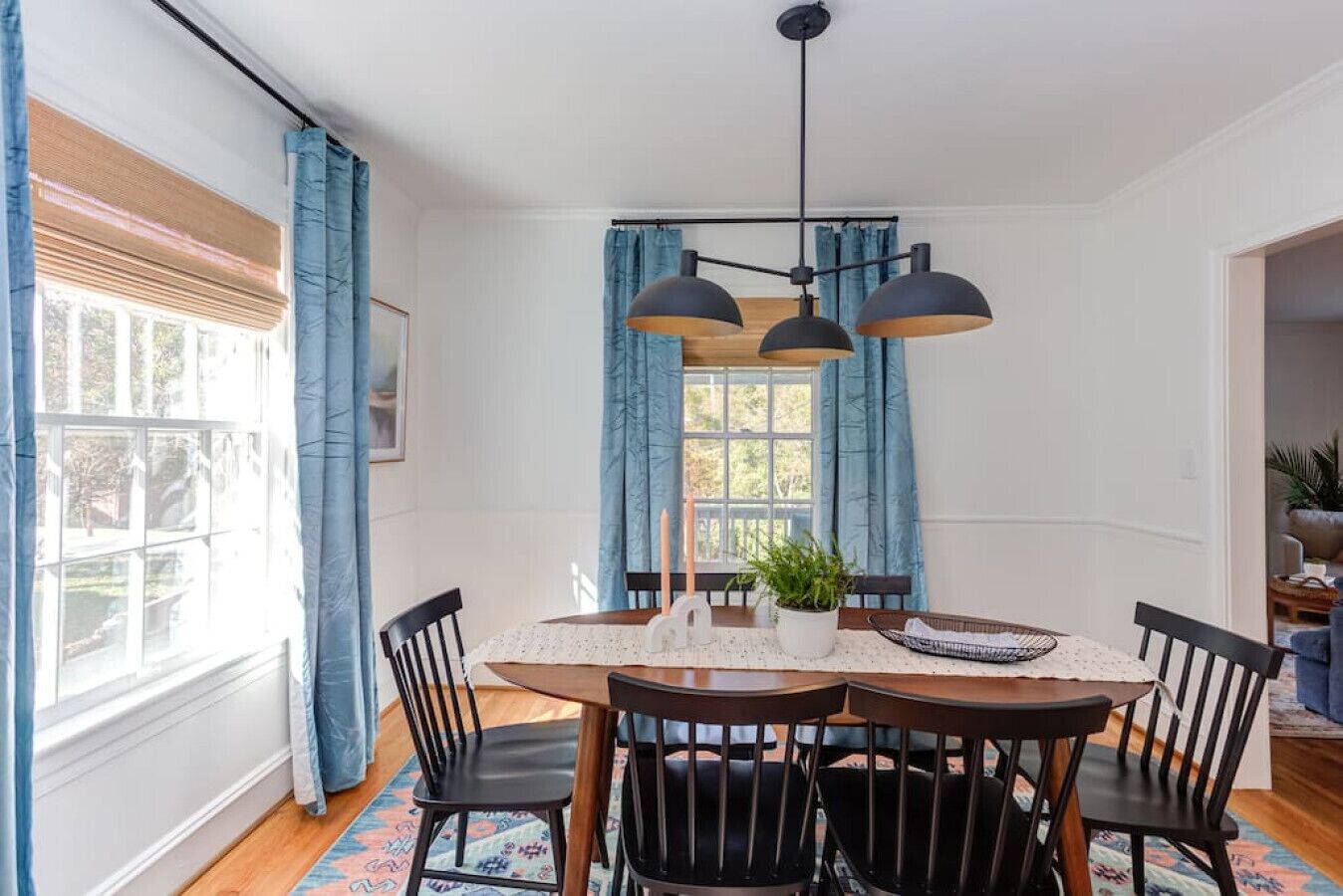 A dining room with a wooden table, black chairs, and a hanging light fixture.