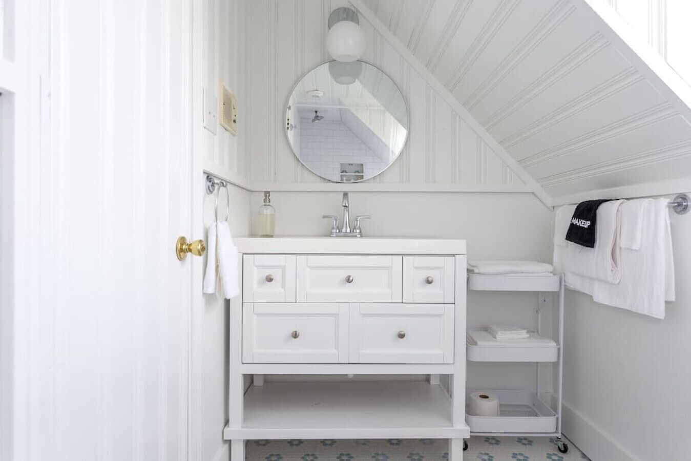 A white bathroom with a vanity, a round mirror, a towel rack, and a toilet.