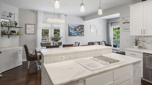 A modern kitchen with a central island, pendant lighting, and a dining area with chairs and a table.