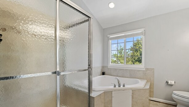 Ein Badezimmer mit Duschkabine aus Glas, einer Badewanne, einer Toilette und einem Fenster mit Blick auf Bäume.