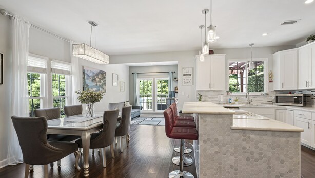 A modern kitchen with white cabinets, a central island, and a dining area with a table and chairs.