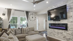 A modern living room with a sectional sofa, a flat-screen TV mounted on a stone wall, and a fireplace.