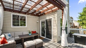 A covered patio with a wooden deck, outdoor furniture, and a sliding glass door.