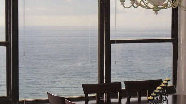 A dining area with a view of the sea through large windows, a chandelier, and a candle holder on the table. - Oceanfront dream condo 2/2 (Hollywood)