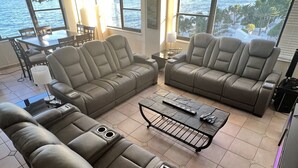 A spacious living area with a large sectional sofa, a coffee table, and a dining table. The room has large windows offering a view of the ocean. - Oceanfront dream condo 2/2 (Hollywood)