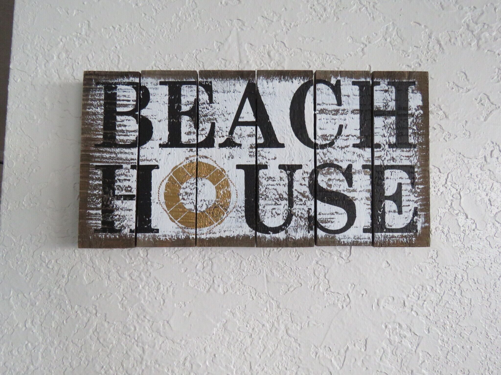 Une enseigne en bois sur laquelle on peut lire, en grandes lettres vieillies, les mots « BEACH HOUSE ».