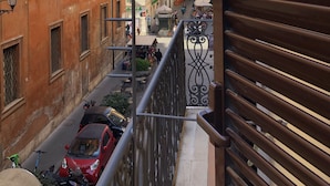 Une rue étroite, bordée de bâtiments des deux côtés, avec un trottoir pour les piétons et quelques véhicules garés.