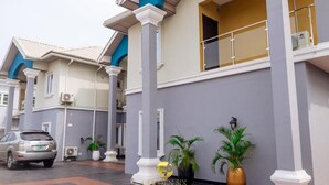 A hotel entrance with a car parked in front, a potted plant, and a sign for the Golden Six Hotel & Restaurant. - Golden Six Hotel & Restaurant (Lekki)