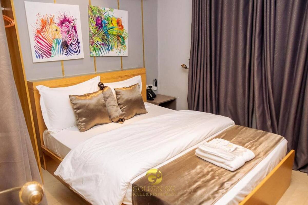 A hotel room with a bed, pillows, a nightstand, and artwork on the wall.