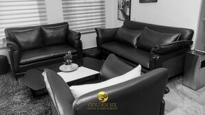 A modern living room with a black leather sofa set, a coffee table with a decorative item, and a small side table. - Golden Six Hotel & Restaurant (Lekki)