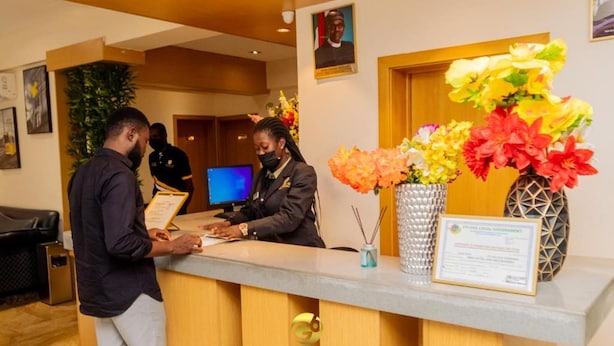 A hotel reception desk with a monitor, a framed certificate, and a vase of flowers. - Golden Six Hotel & Restaurant (Lekki)