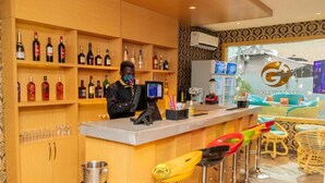 A bar area with shelves of liquor bottles, a counter with a digital screen, and colorful bar stools. - Golden Six Hotel & Restaurant (Lekki)