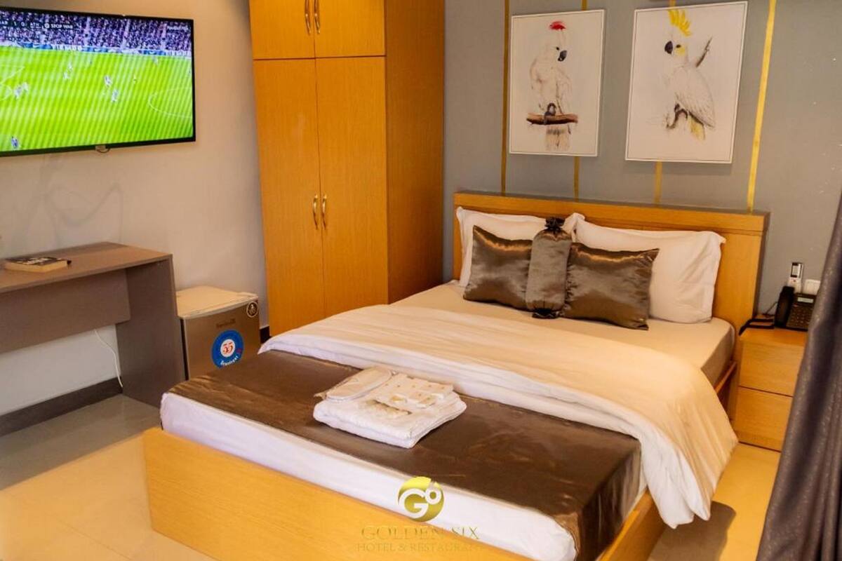 A hotel room with a bed, a TV, a desk, and artwork on the wall.