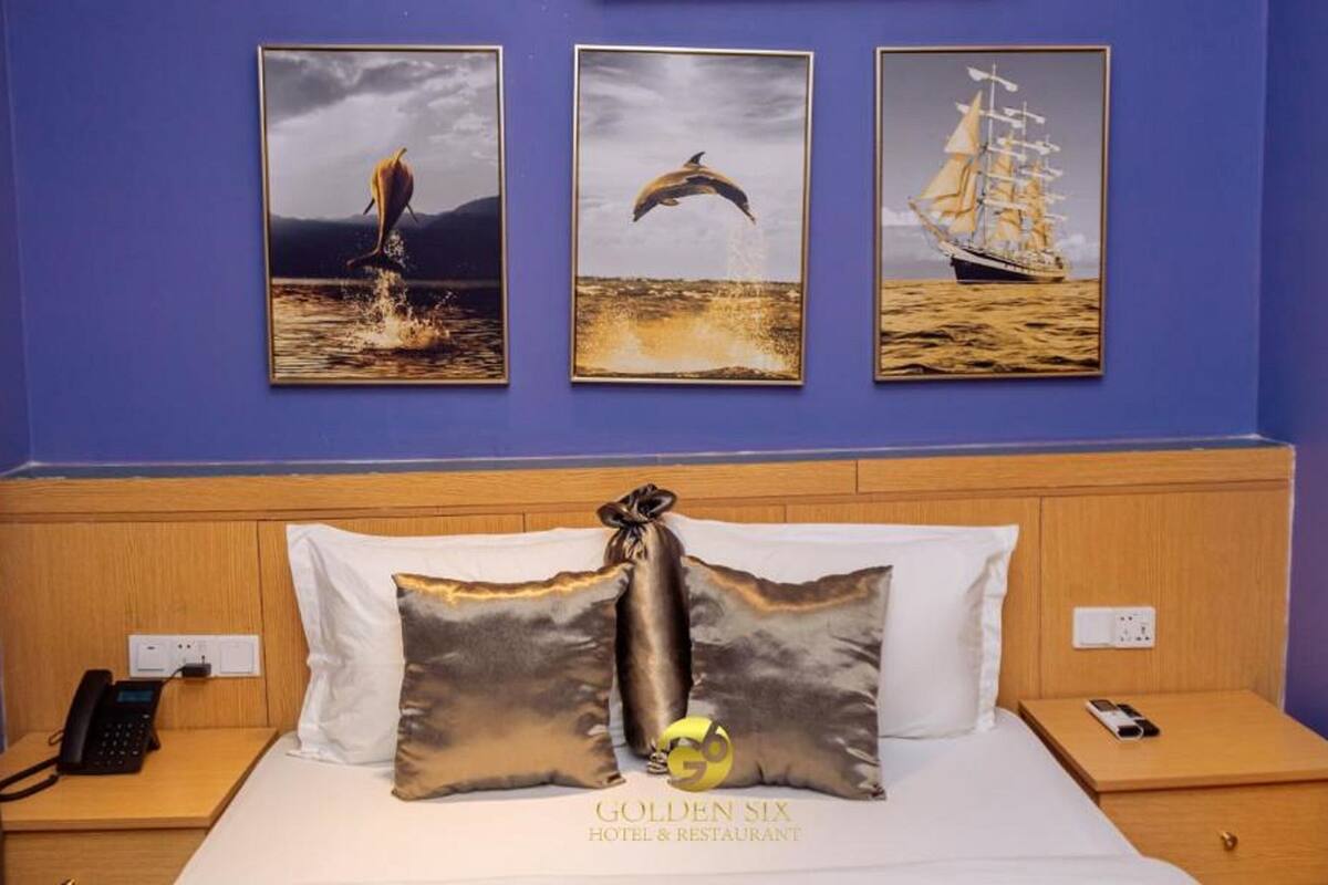 A hotel room with a bed, a bedside phone, and three framed pictures on the wall.