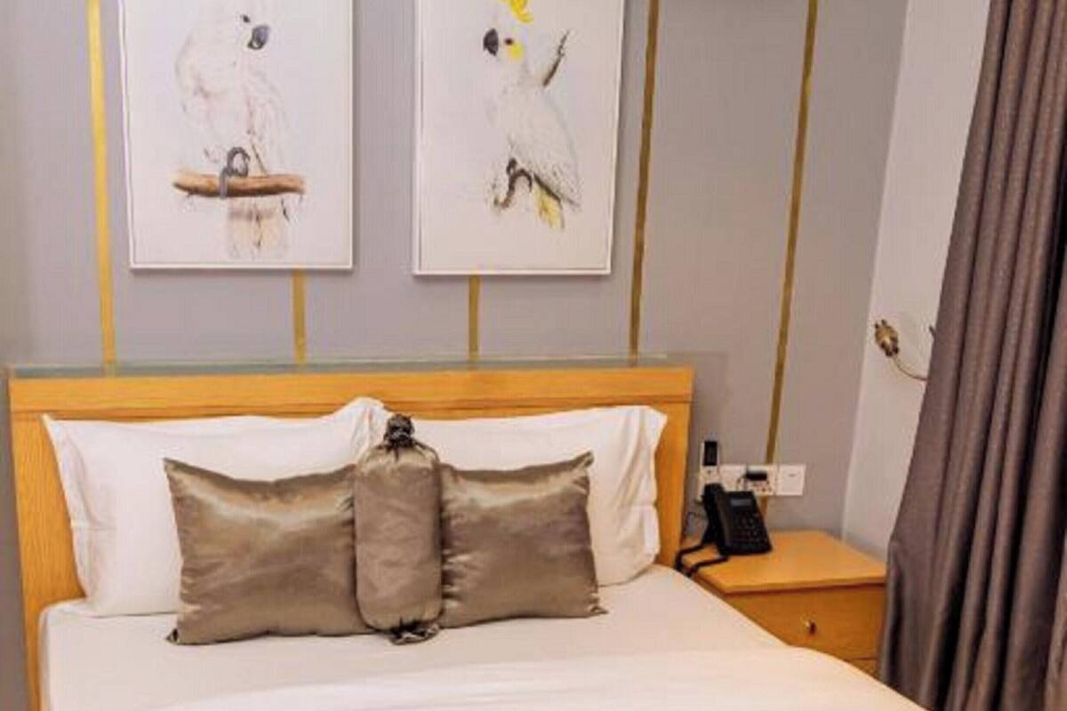 A hotel room with a bed, pillows, a bedside table with a phone, and two wall-mounted air conditioning units.