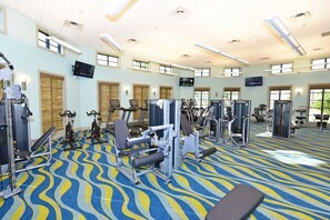 A gym with various exercise machines, a patterned carpet, and large windows allowing natural light. - Lovely Champions Gate Home with Game Room (Davenport)