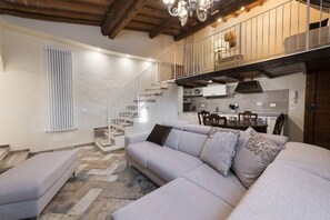 A modern living room with a sofa, a dining table, and a staircase leading to an upper level. - Casa Griselda by Mmega (Florence)