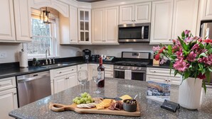Une cuisine avec des armoires blanches, un comptoir en granit, une machine à café, un four à micro-ondes, une cuisinière et un vase rempli de fleurs.