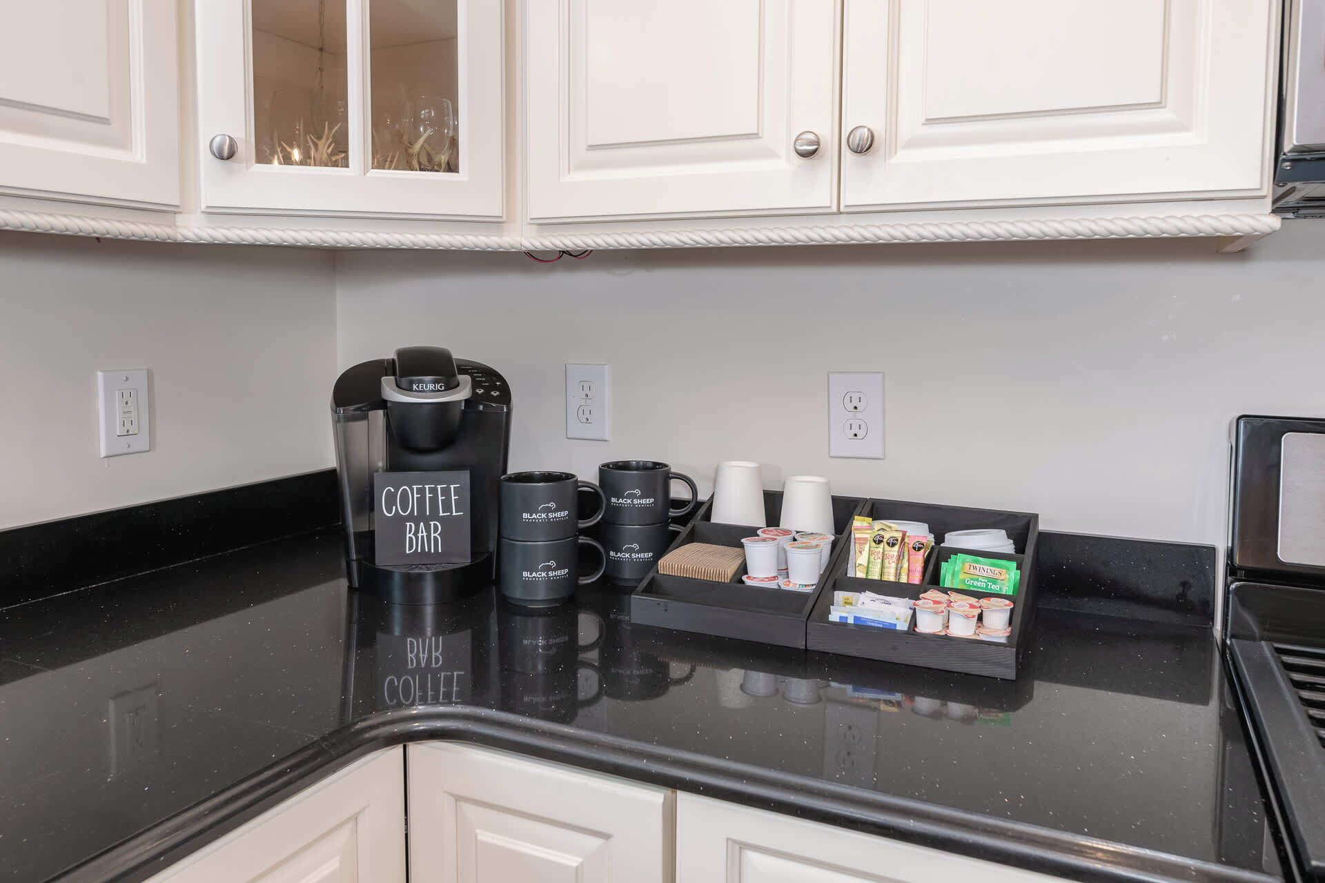 Een kitchenette met een koffiezetapparaat, mokken en een bakje koffiecups.