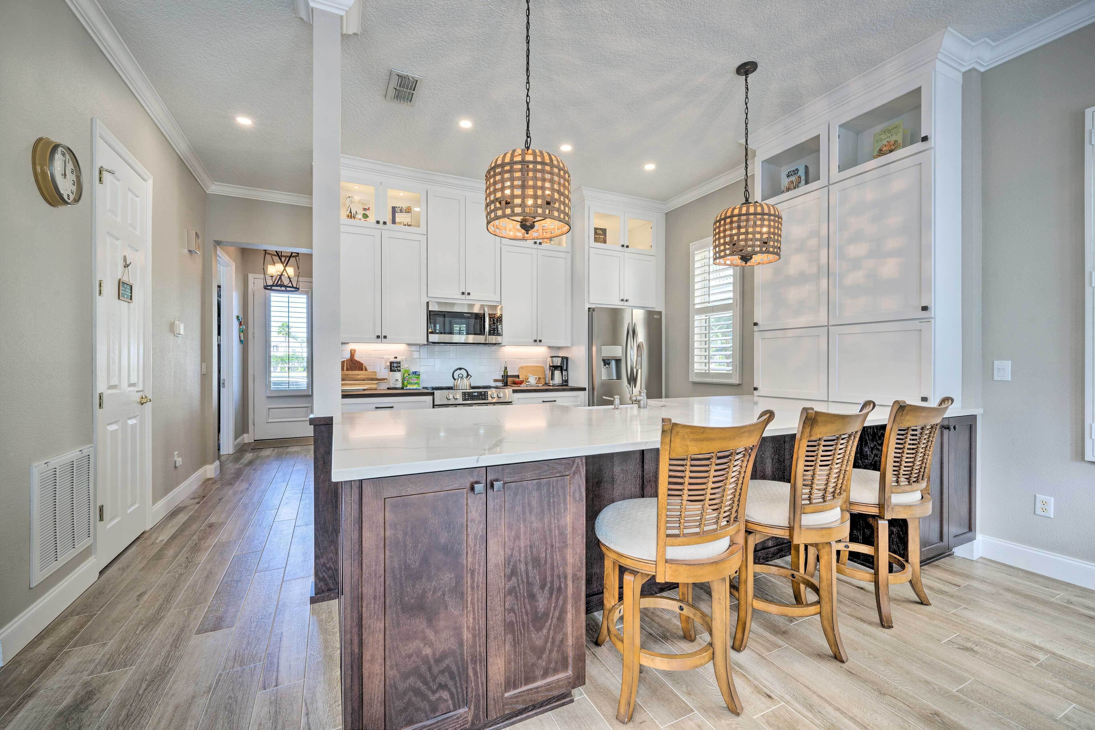 A spacious kitchen with a large island, wooden chairs, and pendant lighting.