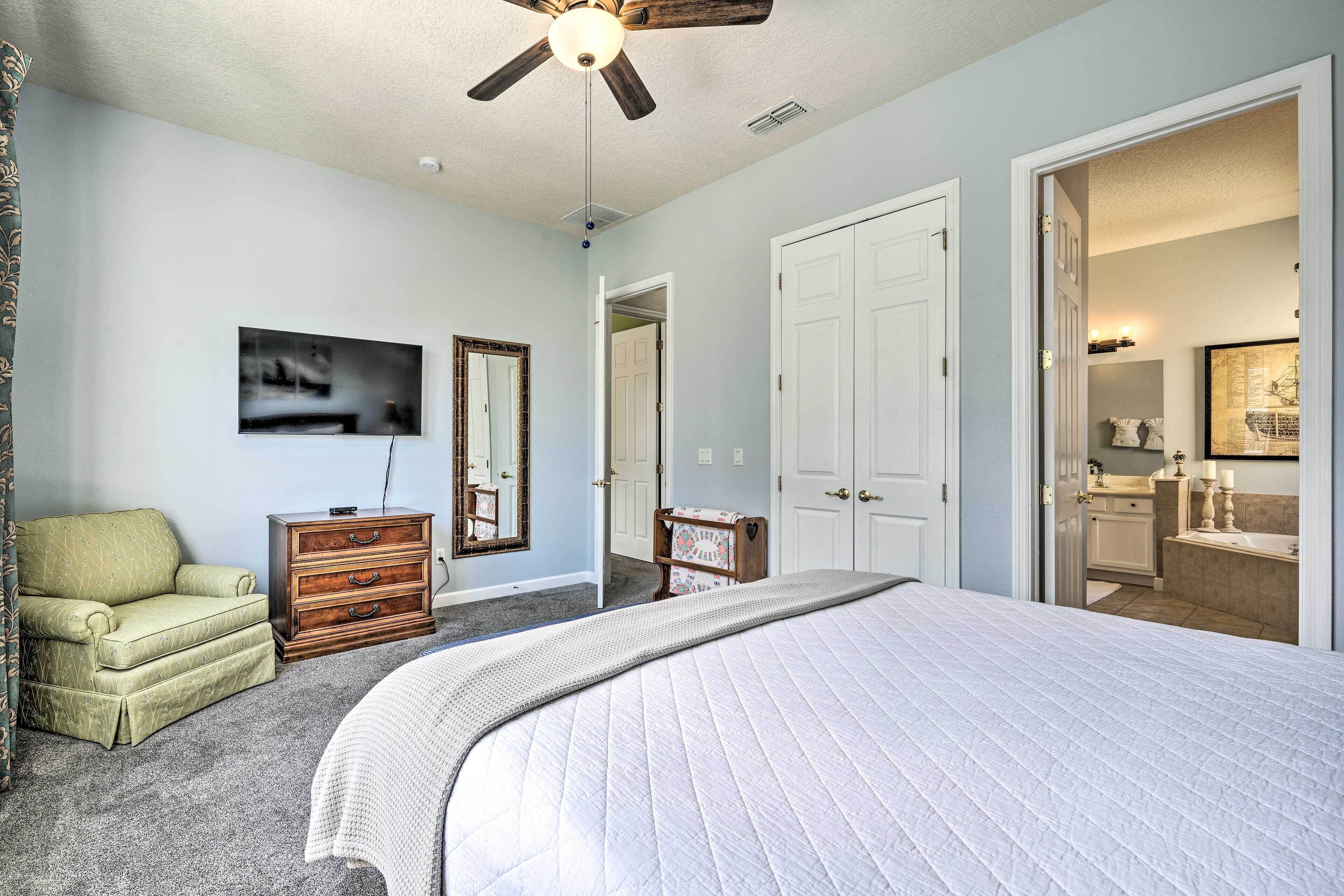 A bedroom with a bed, a chair, a dresser, a ceiling fan, and a door leading to a bathroom.