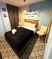 Une chambre d’hôtel avec un lit, une chaise, un mur orné d’une inscription décorative et un sol recouvert de carreaux à motifs.