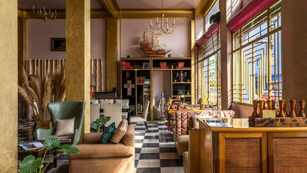 A spacious living room with a checkered floor, a green armchair, a sofa, and a wooden bar area with bowling pins. - Mala Vecindad Centro Historico (Mexico City)