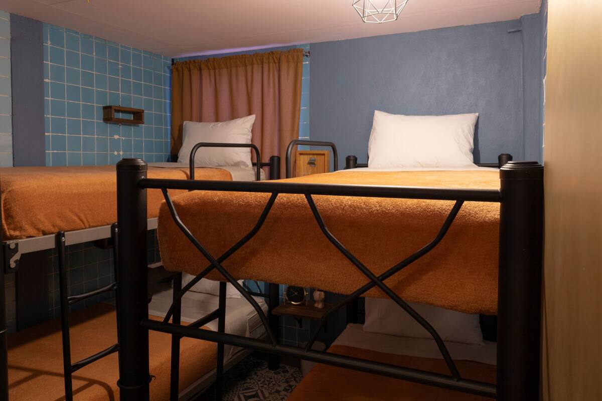 A dormitory room with two beds, a small table, and a clock.