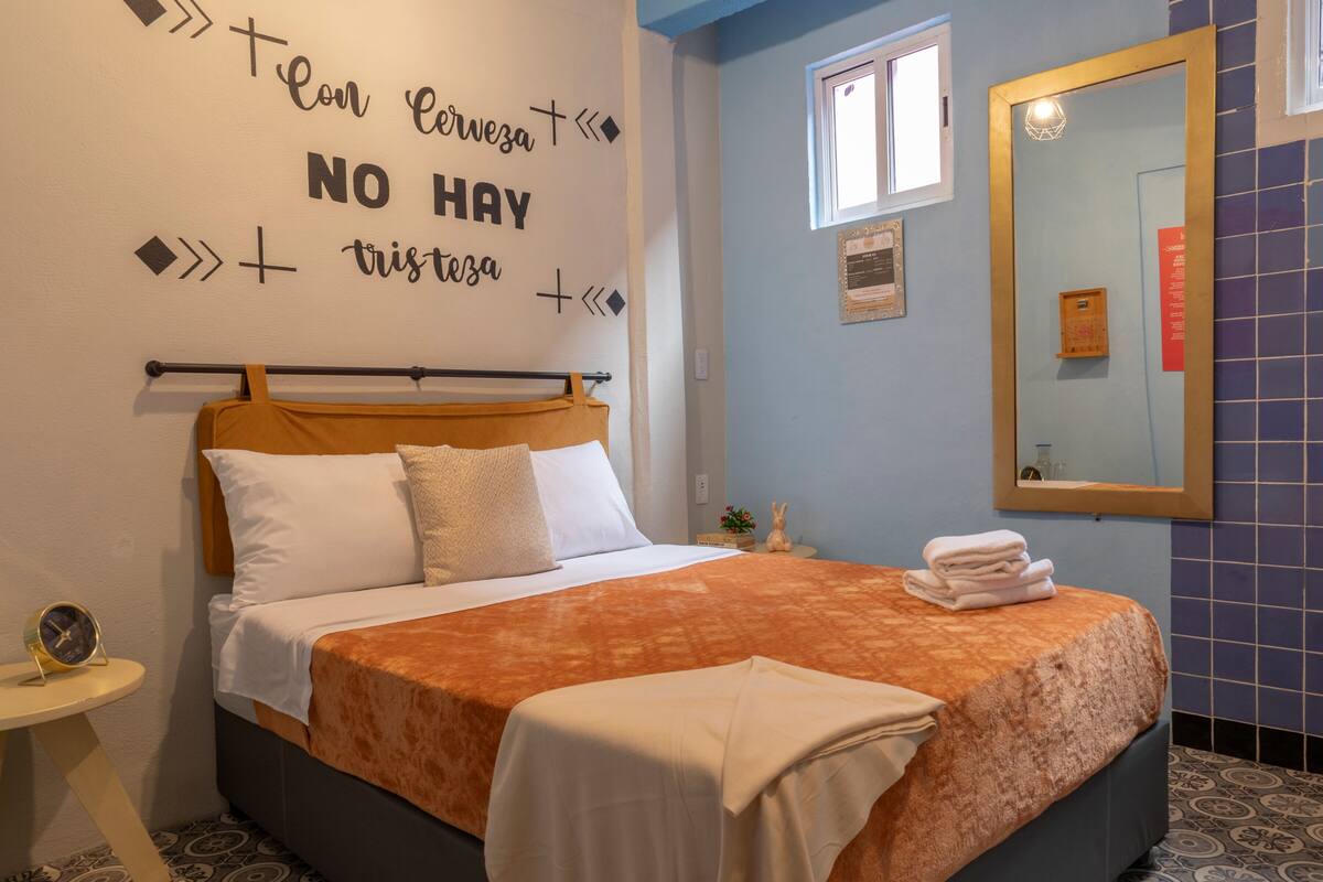 A neatly made bed with a patterned bedspread, a bedside table with a clock, and a wall with a motivational quote.