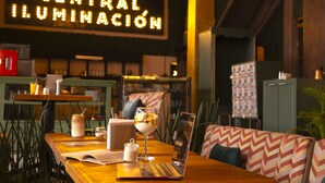A cozy restaurant interior with a wooden table, a laptop, a dessert, and a neon sign reading "CENTRAL ILUMINACIÓN". - Mala Vecindad Centro Historico (Mexico City)