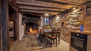 Comedor con suelo de piedra, chimenea, vigas de madera y pared de piedra.