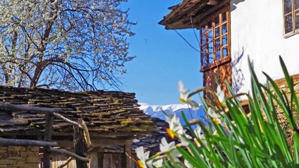 Un edificio rústico con pared de piedra y vigas de madera, cerca de madera y cielo azul despejado.