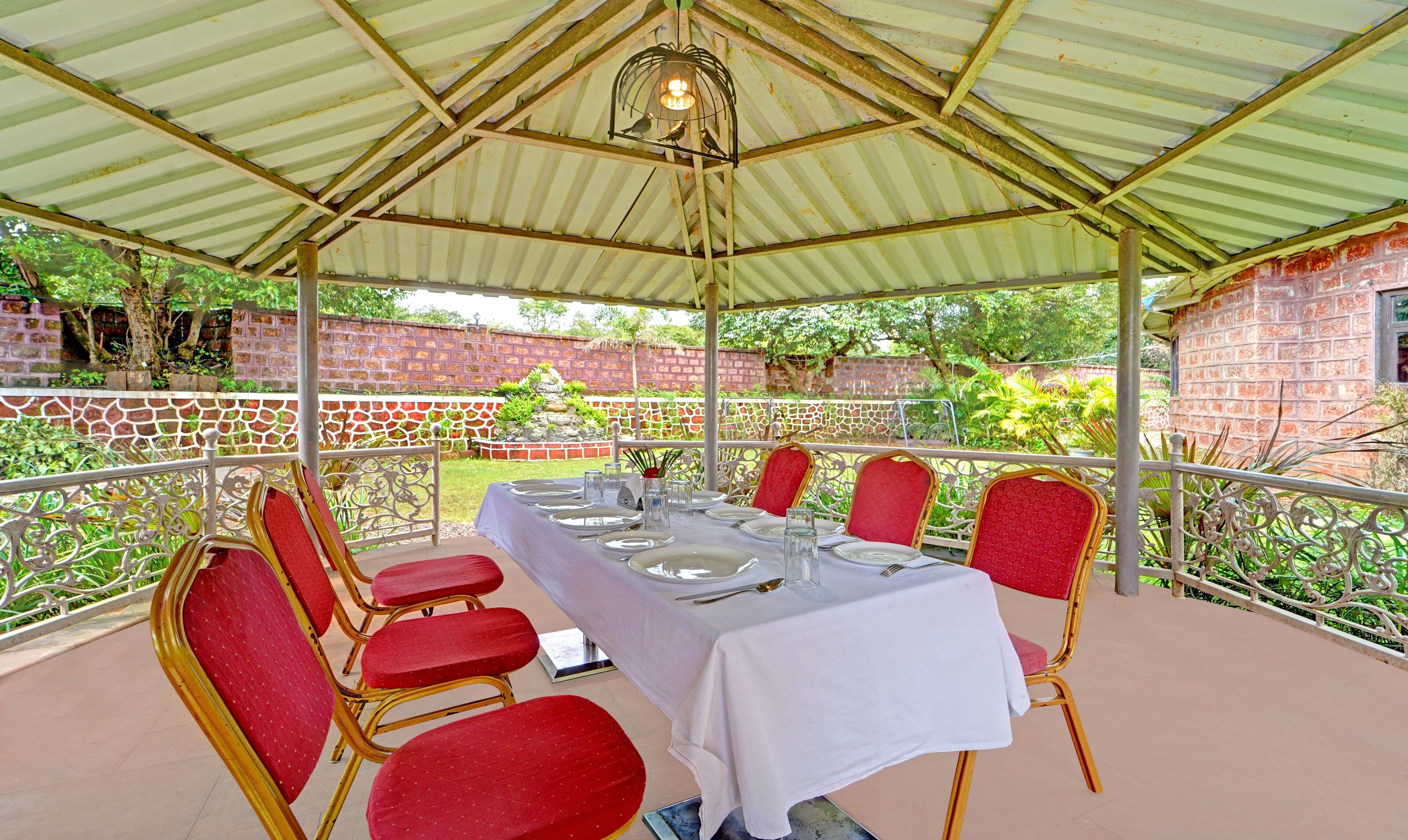 Un espace de restauration extérieur abrité, avec une table dressée pour six personnes, entourée de chaises à revêtement rouge.