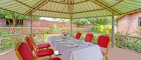 Un espace de restauration extérieur abrité, avec une table dressée pour six personnes, entourée de chaises à revêtement rouge.