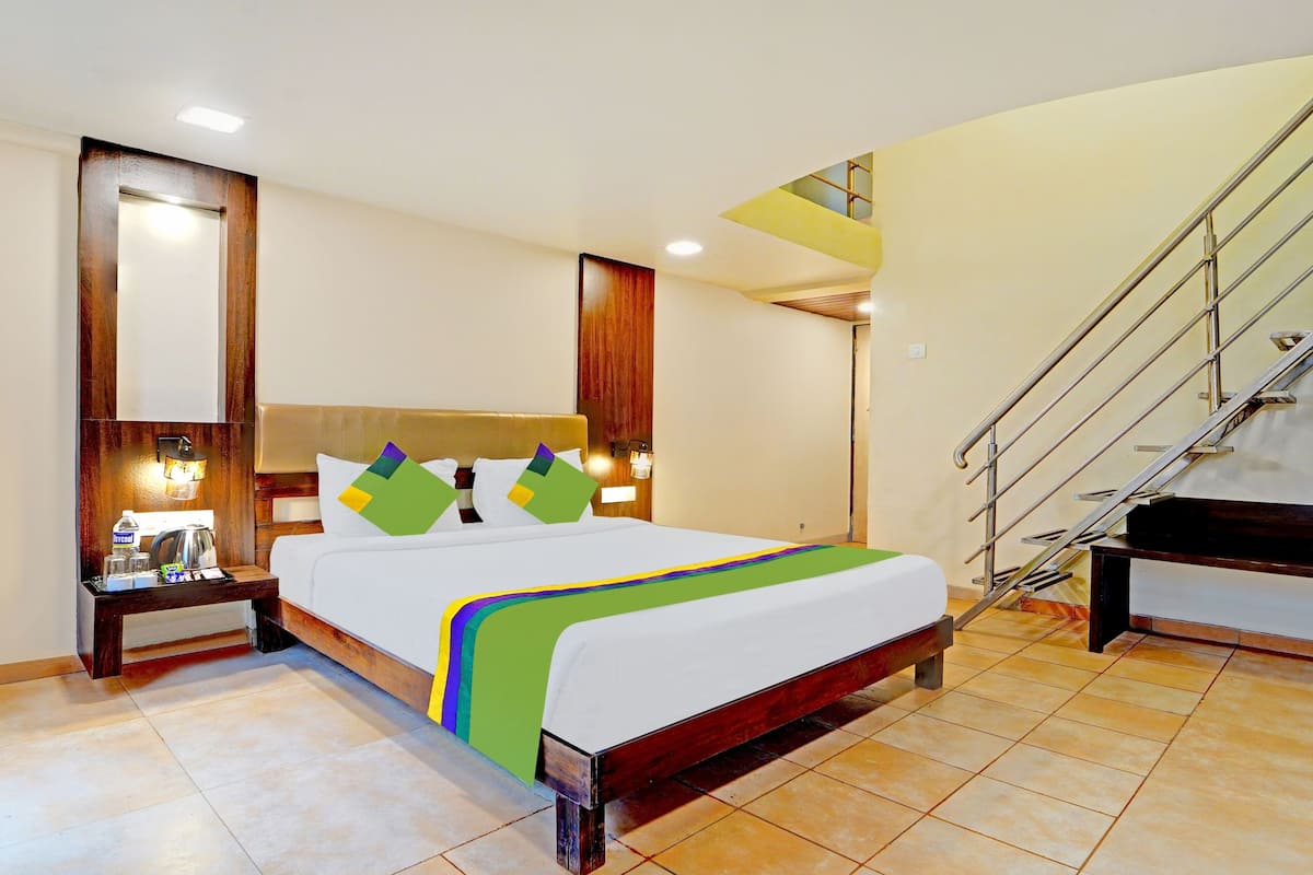 Quarto de hotel com cama, mesas de cabeceira, abajur, escada e vista para o exterior.
